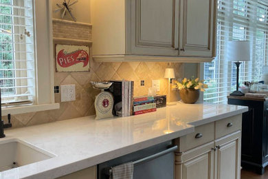 Elegant kitchen photo with an undermount sink, raised-panel cabinets, quartz countertops, beige backsplash, stone tile backsplash, stainless steel appliances and white countertops