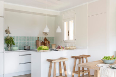 Beach style u-shaped kitchen in Other with flat-panel cabinets, white cabinets, blue splashback, medium hardwood floors, a peninsula, brown floor and white benchtop.