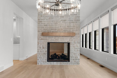 Example of a large transitional light wood floor and brown floor enclosed dining room design in Other with white walls, a two-sided fireplace and a stone fireplace