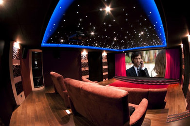 Modelo de cine en casa cerrado actual grande con paredes negras, suelo de madera clara, pantalla de proyección y suelo marrón