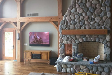 Photo of a mid-sized country enclosed living room in Grand Rapids with grey walls, dark hardwood floors, a standard fireplace, a stone fireplace surround, a wall-mounted tv and brown floor.