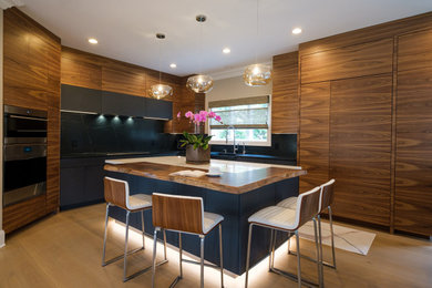 Inspiration for a large contemporary l-shaped light wood floor eat-in kitchen remodel in New York with an integrated sink, flat-panel cabinets, medium tone wood cabinets, marble countertops, black backsplash, stone slab backsplash, paneled appliances, an island and black countertops