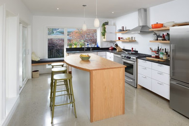 Minimalist l-shaped concrete floor kitchen photo in Toronto with an undermount sink, flat-panel cabinets, white cabinets, solid surface countertops, black backsplash, stainless steel appliances and an island