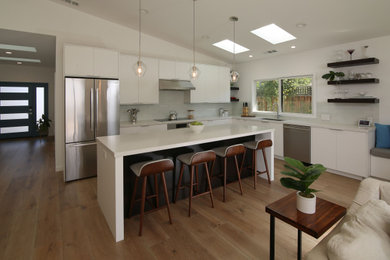 Eat-in kitchen - huge contemporary l-shaped medium tone wood floor, brown floor and vaulted ceiling eat-in kitchen idea in San Francisco with a single-bowl sink, flat-panel cabinets, white cabinets, quartz countertops, white backsplash, glass tile backsplash, stainless steel appliances, an island and gray countertops
