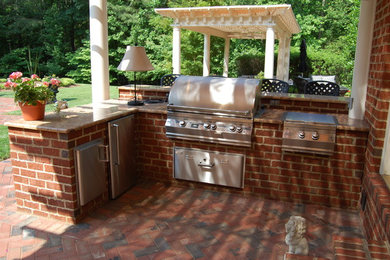 Backyard brick patio kitchen photo in Richmond with a pergola