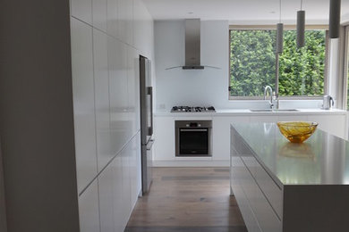 Inspiration for a mid-sized modern l-shaped eat-in kitchen in Sydney with an undermount sink, flat-panel cabinets, white cabinets, quartz benchtops, white splashback, stainless steel appliances, ceramic floors, with island and glass sheet splashback.