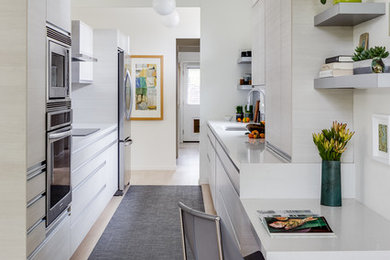 Inspiration for a mid-sized midcentury galley eat-in kitchen in San Francisco with light hardwood floors, beige floor, an undermount sink, flat-panel cabinets, stainless steel appliances, solid surface benchtops, white cabinets, white benchtop, multi-coloured splashback, mosaic tile splashback and timber.