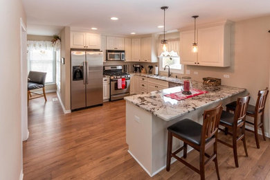 This is an example of a mid-sized traditional u-shaped eat-in kitchen in Chicago with a single-bowl sink, raised-panel cabinets, white cabinets, granite benchtops, stainless steel appliances and a peninsula.
