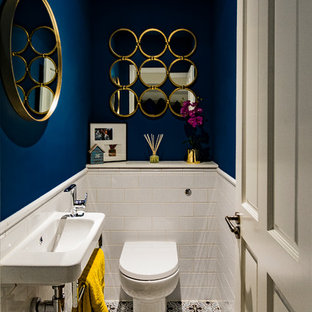 This is an example of a contemporary cloakroom in London with a one-piece toilet, white tiles, blue walls, cement flooring, a wall-mounted sink and multi-coloured floors.