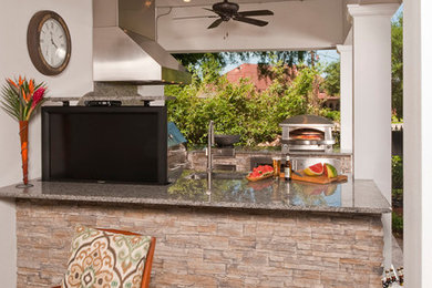 Large elegant backyard stone patio kitchen photo in New Orleans with a roof extension