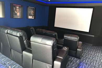 This is an example of a mid-sized transitional enclosed home theatre in Orlando with blue walls, carpet, a projector screen and grey floor.