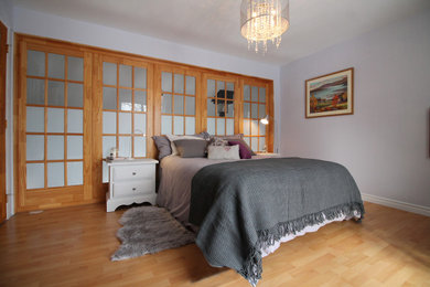 Mid-sized trendy master laminate floor, beige floor and wood wall bedroom photo in Other with gray walls and a standard fireplace