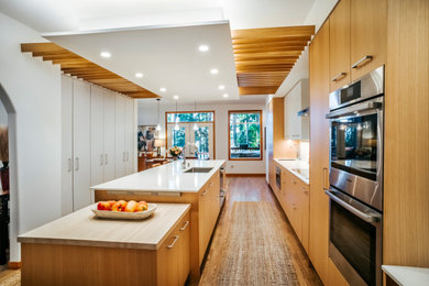 Photo of a scandinavian galley kitchen in Seattle with an undermount sink, flat-panel cabinets, light wood cabinets, quartz benchtops, white splashback, ceramic splashback, stainless steel appliances, light hardwood floors, with island, white benchtop and exposed beam.