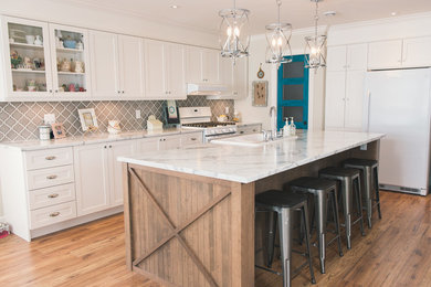 Example of a large arts and crafts l-shaped medium tone wood floor eat-in kitchen design in Other with a farmhouse sink, shaker cabinets, white cabinets, laminate countertops, gray backsplash, ceramic backsplash, white appliances, an island and white countertops