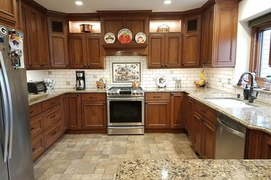 Example of a mid-sized classic u-shaped porcelain tile and brown floor kitchen design in Other with an undermount sink, beaded inset cabinets, medium tone wood cabinets, granite countertops, white backsplash, subway tile backsplash, stainless steel appliances and a peninsula