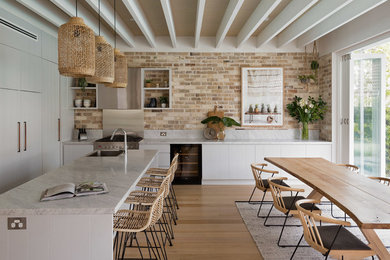 Inspiration for a beach style l-shaped eat-in kitchen in Sydney with a drop-in sink, flat-panel cabinets, white cabinets, brick splashback, stainless steel appliances, light hardwood floors and with island.