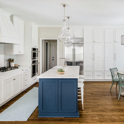 Mid-sized transitional l-shaped medium tone wood floor and brown floor eat-in kitchen photo in Charlotte with a farmhouse sink, shaker cabinets, white cabinets, quartz countertops, gray backsplash, porcelain backsplash, stainless steel appliances, an island and white countertops