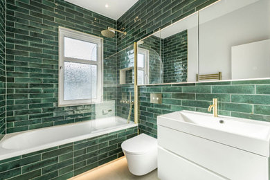 Design ideas for a small contemporary family bathroom in London with white cabinets, a built-in bath, a shower/bath combination, a wall mounted toilet, green tiles, ceramic tiles, white walls, ceramic flooring, a built-in sink, beige floors, a wall niche, a single sink and a floating vanity unit.