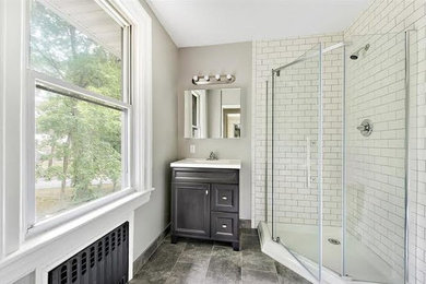 Example of a transitional white tile and subway tile porcelain tile and gray floor corner shower design in New York with furniture-like cabinets, dark wood cabinets, gray walls, an undermount sink, quartz countertops and a hinged shower door