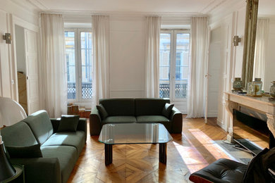 パリにある高級な中くらいなトランジショナルスタイルのおしゃれな独立型リビング (白い壁、淡色無垢フローリング、標準型暖炉、石材の暖炉まわり、テレビなし、茶色い床) の写真