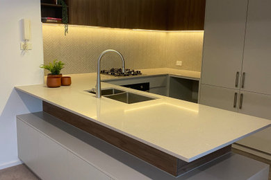 Photo of a mid-sized contemporary u-shaped eat-in kitchen in Melbourne with an undermount sink, beaded inset cabinets, grey cabinets, quartz benchtops, grey splashback, stone tile splashback, panelled appliances, laminate floors, with island, brown floor and grey benchtop.