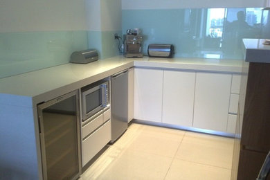 This is an example of a small modern u-shaped kitchen in Sydney with flat-panel cabinets, white cabinets, blue splashback, glass sheet splashback, stainless steel appliances and no island.