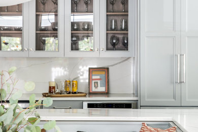 ポートランド(メイン)にある高級な広いトランジショナルスタイルのおしゃれなキッチン (アンダーカウンターシンク、フラットパネル扉のキャビネット、グレーのキャビネット、クオーツストーンカウンター、マルチカラーのキッチンパネル、石タイルのキッチンパネル、パネルと同色の調理設備、濃色無垢フローリング、茶色い床、白いキッチンカウンター) の写真