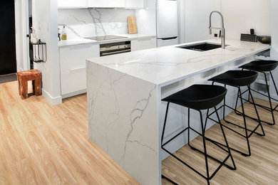 Open concept kitchen - mid-sized modern galley light wood floor open concept kitchen idea in Vancouver with an undermount sink, flat-panel cabinets, white cabinets, white backsplash, marble backsplash, white appliances and a peninsula