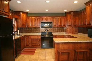 Mid-sized elegant u-shaped travertine floor and beige floor enclosed kitchen photo in Other with an undermount sink, dark wood cabinets, granite countertops, metallic backsplash, mosaic tile backsplash, raised-panel cabinets, black appliances and a peninsula