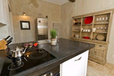 Mid-sized country single-wall open plan kitchen in Marseille with an undermount sink, flat-panel cabinets, white cabinets, concrete benchtops, beige splashback, stone tile splashback, panelled appliances, travertine floors and with island.