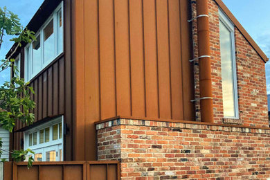 Photo of a small two-storey red house exterior in Other with metal siding, a gable roof, a metal roof and a red roof.