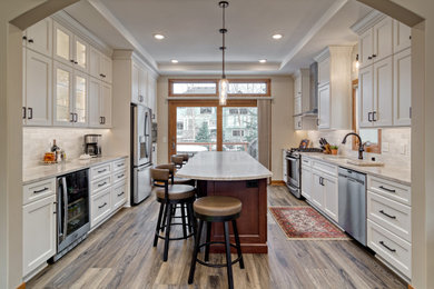 Mid-sized elegant u-shaped vinyl floor, brown floor and tray ceiling eat-in kitchen photo in Minneapolis with an undermount sink, flat-panel cabinets, white cabinets, quartzite countertops, white backsplash, ceramic backsplash, stainless steel appliances, an island and beige countertops