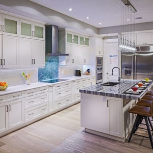 This is an example of a large transitional l-shaped kitchen pantry in Calgary with a drop-in sink, white cabinets, blue splashback, stainless steel appliances, light hardwood floors, with island and shaker cabinets.