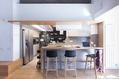 This is an example of a contemporary u-shaped kitchen in Barcelona with a peninsula, flat-panel cabinets, white cabinets, wood benchtops, grey splashback, glass sheet splashback, stainless steel appliances, beige floor and beige benchtop.