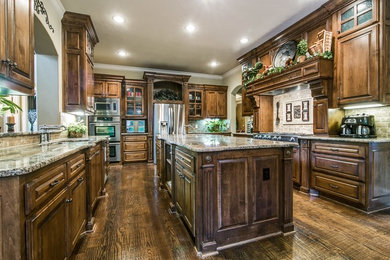 Design ideas for a large traditional u-shaped separate kitchen in Dallas with an undermount sink, raised-panel cabinets, dark wood cabinets, granite benchtops, beige splashback, stone tile splashback, stainless steel appliances, dark hardwood floors and with island.