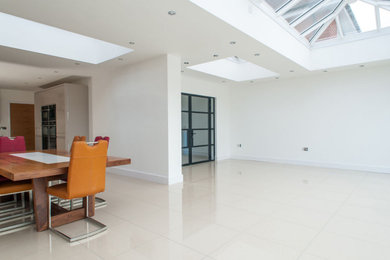 Large modern open plan dining room in London with white walls, ceramic flooring and feature lighting.