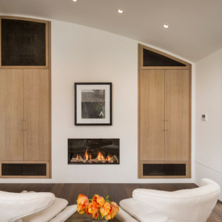 Bild på ett mellanstort funkis hemmabibliotek, med vita väggar, mörkt trägolv, en bred öppen spis, en spiselkrans i gips och ett fristående skrivbord