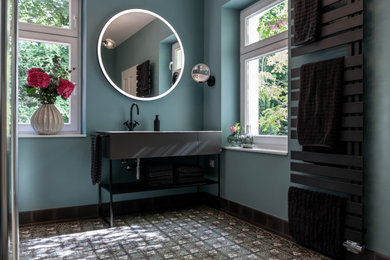 Großes Modernes Badezimmer mit flächenbündigen Schrankfronten, grauen Schränken, Wandtoilette mit Spülkasten, Zementfliesen für Boden, Einbauwaschbecken, Mineralwerkstoff-Waschtisch, türkisem Boden, weißer Waschtischplatte, Einzelwaschbecken und freistehendem Waschtisch in Sonstige