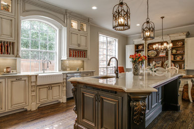 Design ideas for a large traditional l-shaped open plan kitchen in Dallas with a farmhouse sink, white cabinets, marble benchtops, beige splashback, subway tile splashback, stainless steel appliances, dark hardwood floors, with island, raised-panel cabinets and brown floor.