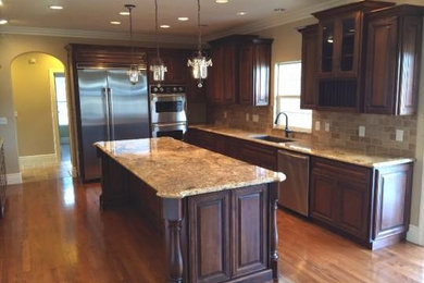 Elegant dark wood floor enclosed kitchen photo in Sacramento with an undermount sink, raised-panel cabinets, dark wood cabinets, granite countertops, beige backsplash, stone tile backsplash, stainless steel appliances and an island