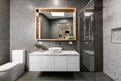 Inspiration for a mid-sized contemporary master gray tile and mosaic tile ceramic tile and gray floor walk-in shower remodel in Los Angeles with white cabinets, gray walls, a vessel sink, marble countertops, a hinged shower door, flat-panel cabinets and white countertops