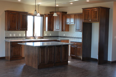 Inspiration for a mid-sized timeless eat-in kitchen remodel in Other with raised-panel cabinets, dark wood cabinets, granite countertops, gray backsplash and an island