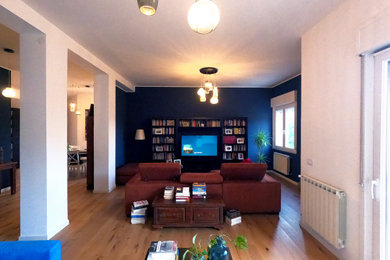 Esempio di un grande soggiorno industriale aperto con libreria, pareti blu, parquet chiaro e TV a parete