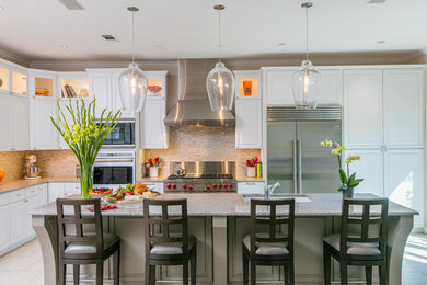 Eat-in kitchen - transitional l-shaped ceramic tile eat-in kitchen idea in Dallas with an undermount sink, raised-panel cabinets, white cabinets, quartz countertops, beige backsplash, stone tile backsplash, stainless steel appliances and an island