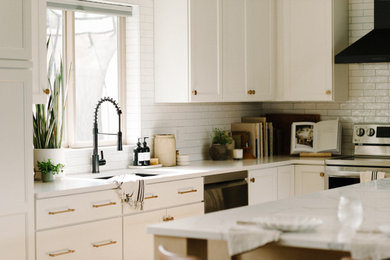 Open concept kitchen - mid-sized transitional l-shaped laminate floor and brown floor open concept kitchen idea in Seattle with an undermount sink, shaker cabinets, white cabinets, quartz countertops, white backsplash, ceramic backsplash, black appliances, an island and white countertops