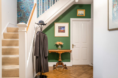 Photo of a medium sized classic foyer in London with green walls, light hardwood flooring, a single front door, a brown front door, brown floors, wallpapered walls and a feature wall.