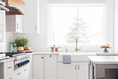 ミネアポリスにある高級な中くらいなトランジショナルスタイルのおしゃれなアイランドキッチン (エプロンフロントシンク、白いキャビネット、シルバーの調理設備、淡色無垢フローリング) の写真