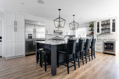 Example of a mid-sized transitional u-shaped medium tone wood floor and brown floor eat-in kitchen design in Other with an undermount sink, recessed-panel cabinets, white cabinets, quartz countertops, white backsplash, stone slab backsplash, stainless steel appliances, an island and white countertops