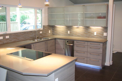 Eat-in kitchen - large contemporary u-shaped porcelain tile eat-in kitchen idea in Austin with an undermount sink, glass-front cabinets, gray cabinets, solid surface countertops, gray backsplash, glass tile backsplash, stainless steel appliances and an island