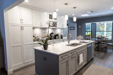 This is an example of a contemporary kitchen/diner in Orlando with a built-in sink, shaker cabinets, grey cabinets, engineered stone countertops, grey splashback, porcelain splashback, stainless steel appliances, an island, brown floors and white worktops.